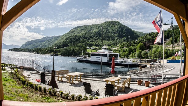 A waterfront view with a boat docked at a pier, outdoor seating, and a mountainous backdrop. - Lavik Fjord Hotell (Hoyanger)