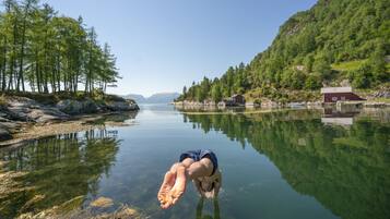 Un lago transparente con una persona buceando en el agua, rodeado de árboles y un pequeño edificio en la orilla.