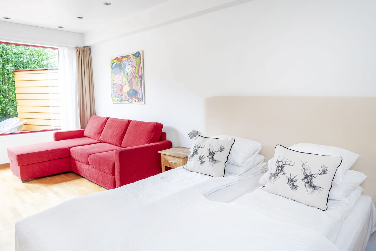 Una camera d'albergo moderna con un letto, un divano rosso e un comodino in legno.
