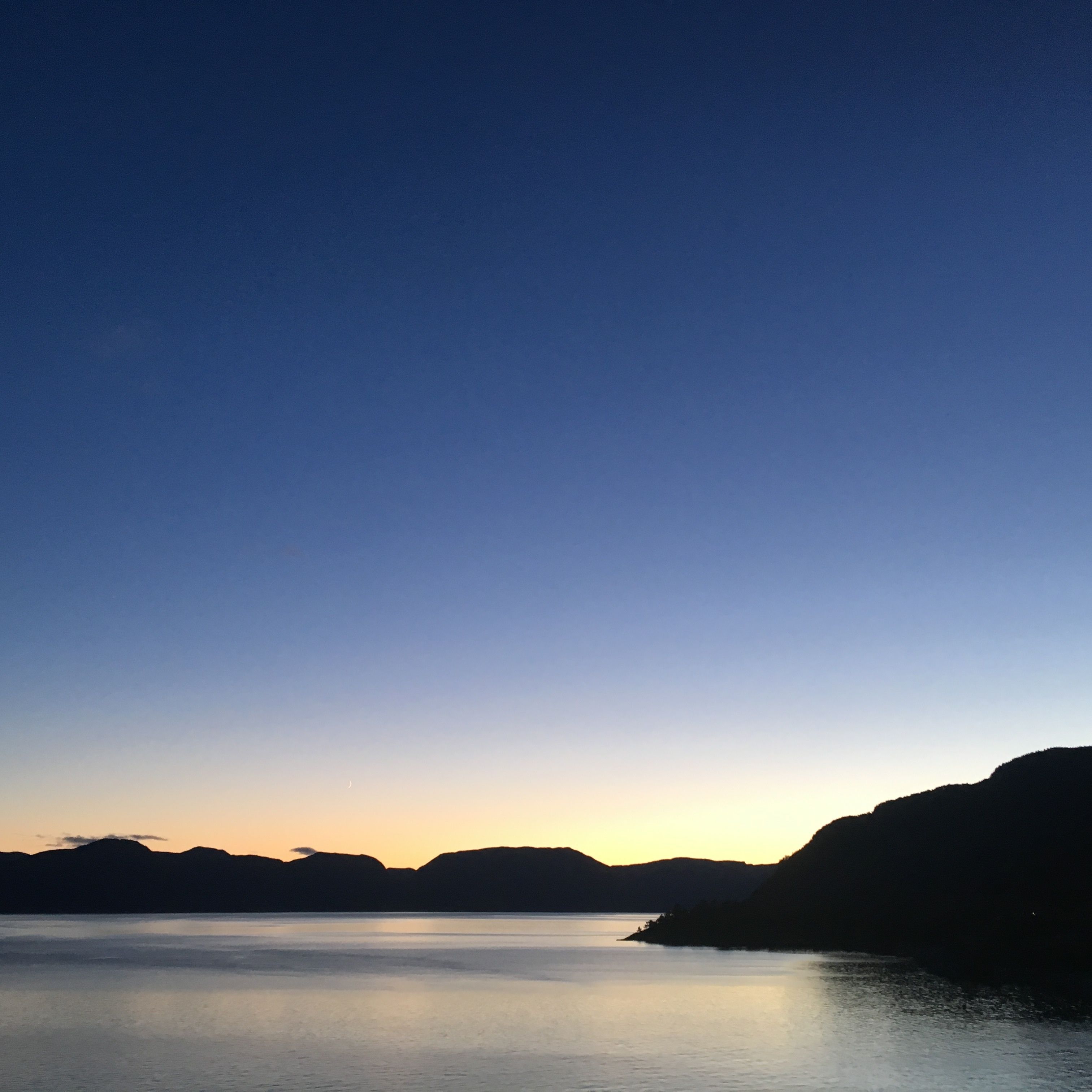 Un lago tranquilo al anochecer con siluetas de montañas al fondo.