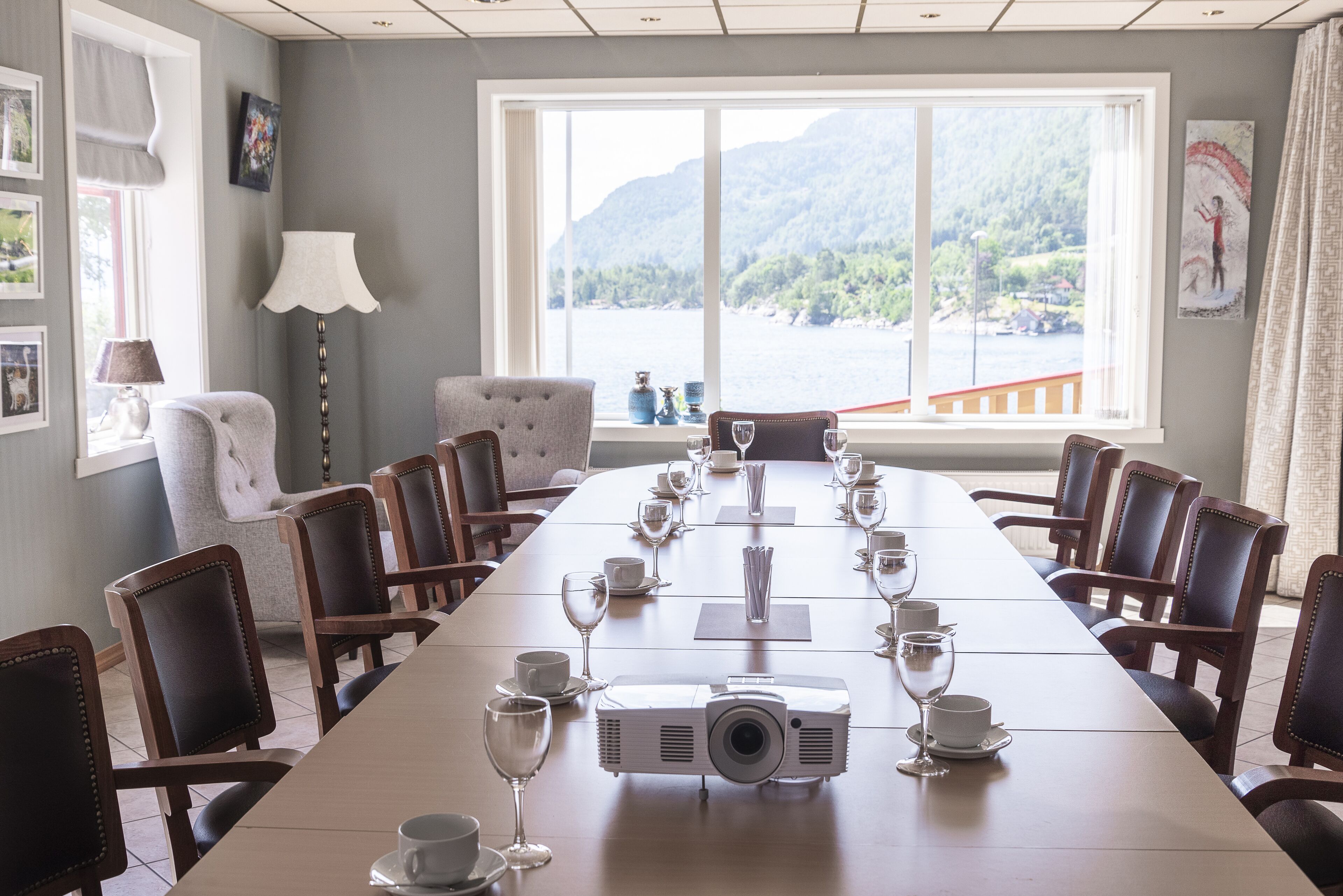 A conference room with a long table set for a meeting, a projector, and a view of a mountainous landscape through large windows.