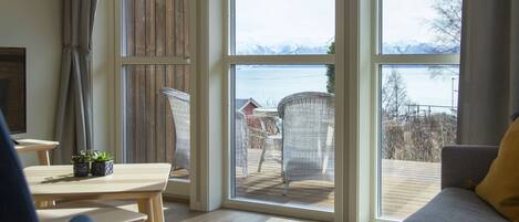 A cozy living room with a large window, wooden flooring, and a view of a deck with outdoor furniture.