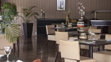 A restaurant with tables set for dining, potted plants, and a grill in the background.