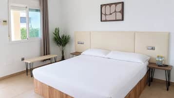 A hotel room with a large bed, a bench, a potted plant, a wall-mounted artwork, and a window with curtains.