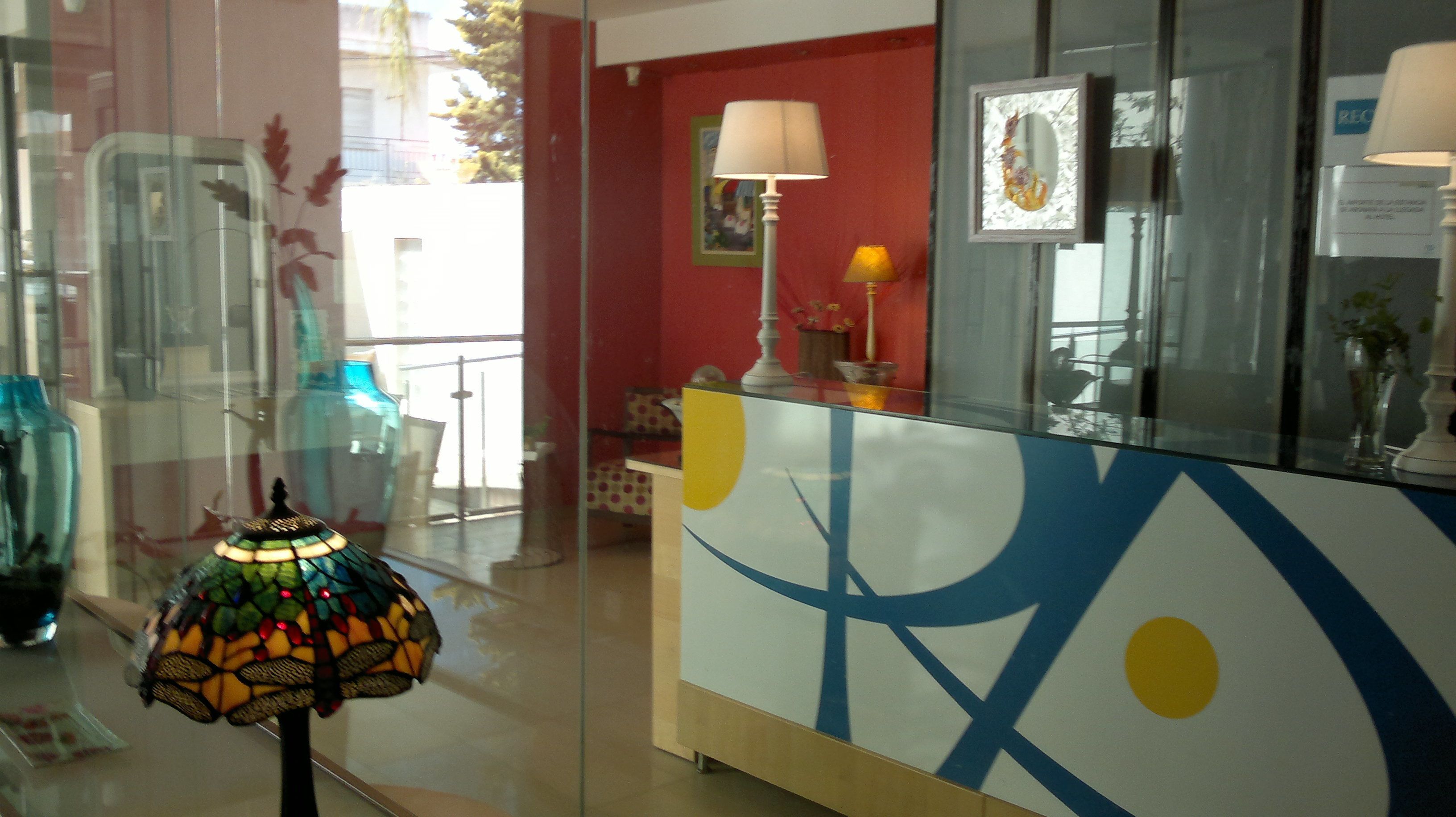 Un área de recepción con separador de vidrio, una lámpara colorida, una pared roja y una obra de arte enmarcada.