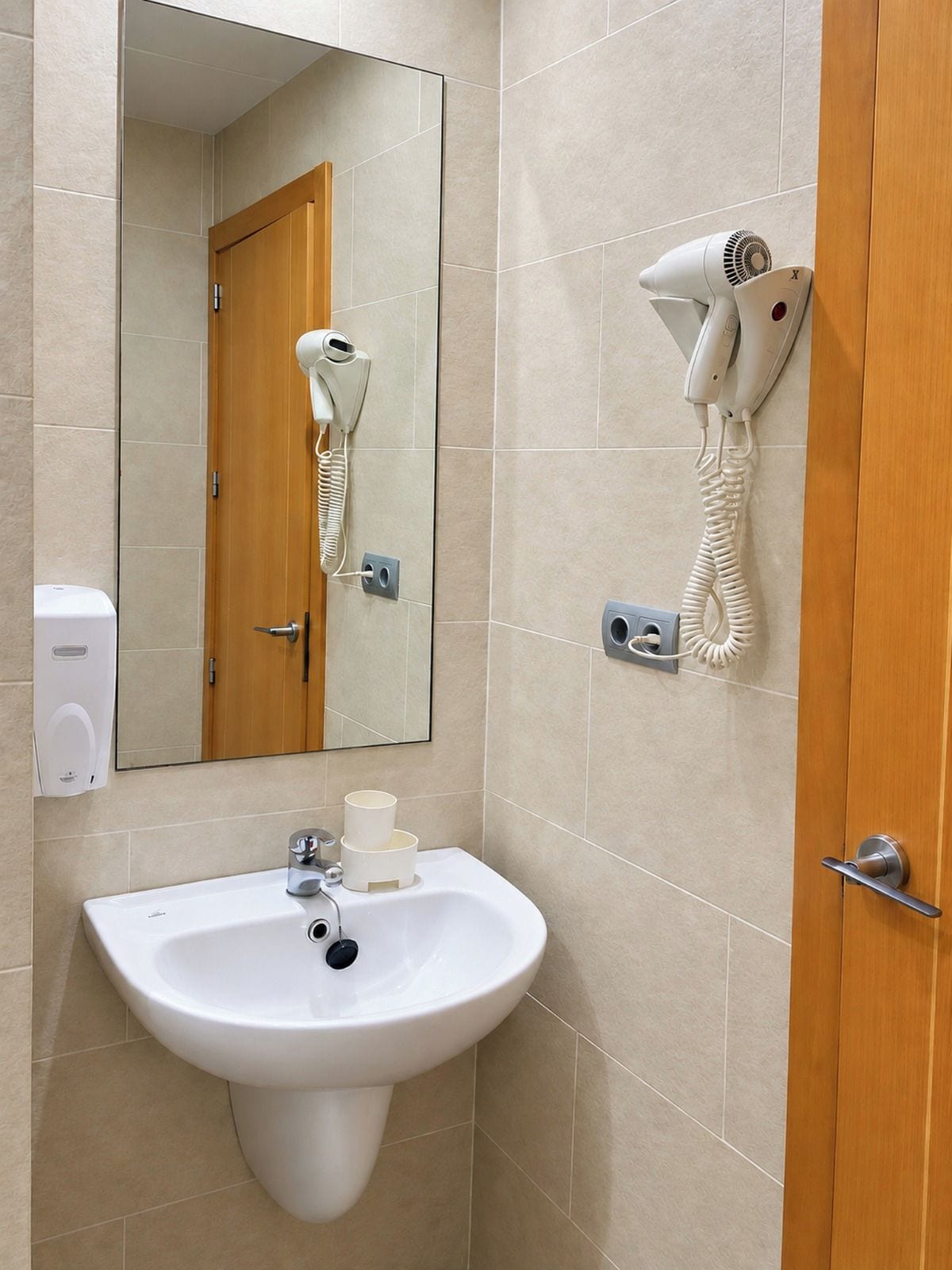 Ein Badezimmer mit einem weißen Waschbecken, einem Spiegel, einem Föhn und einem Handtuchhalter.