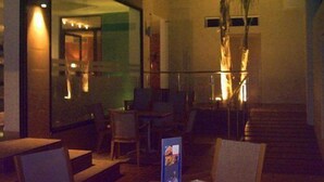 A dimly lit indoor space with a staircase leading to an upper level. There are tables and chairs arranged for seating, and a large plant is visible in the center. - Hotel Playa Terreros by Blossom Hotels (Pulpi)