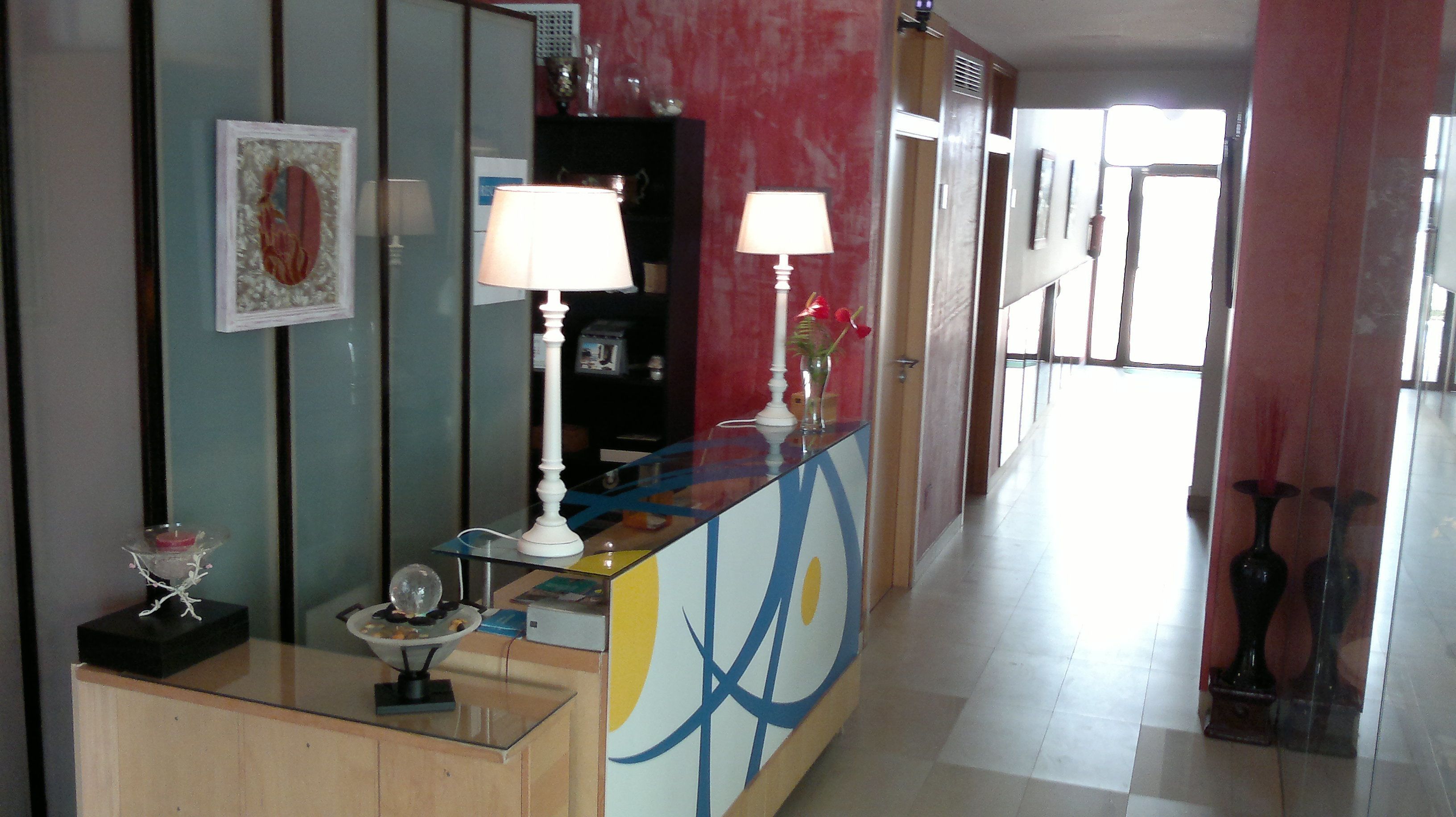 A hotel lobby with a reception desk, a bookshelf, a mirror, and a hallway leading to the exit.