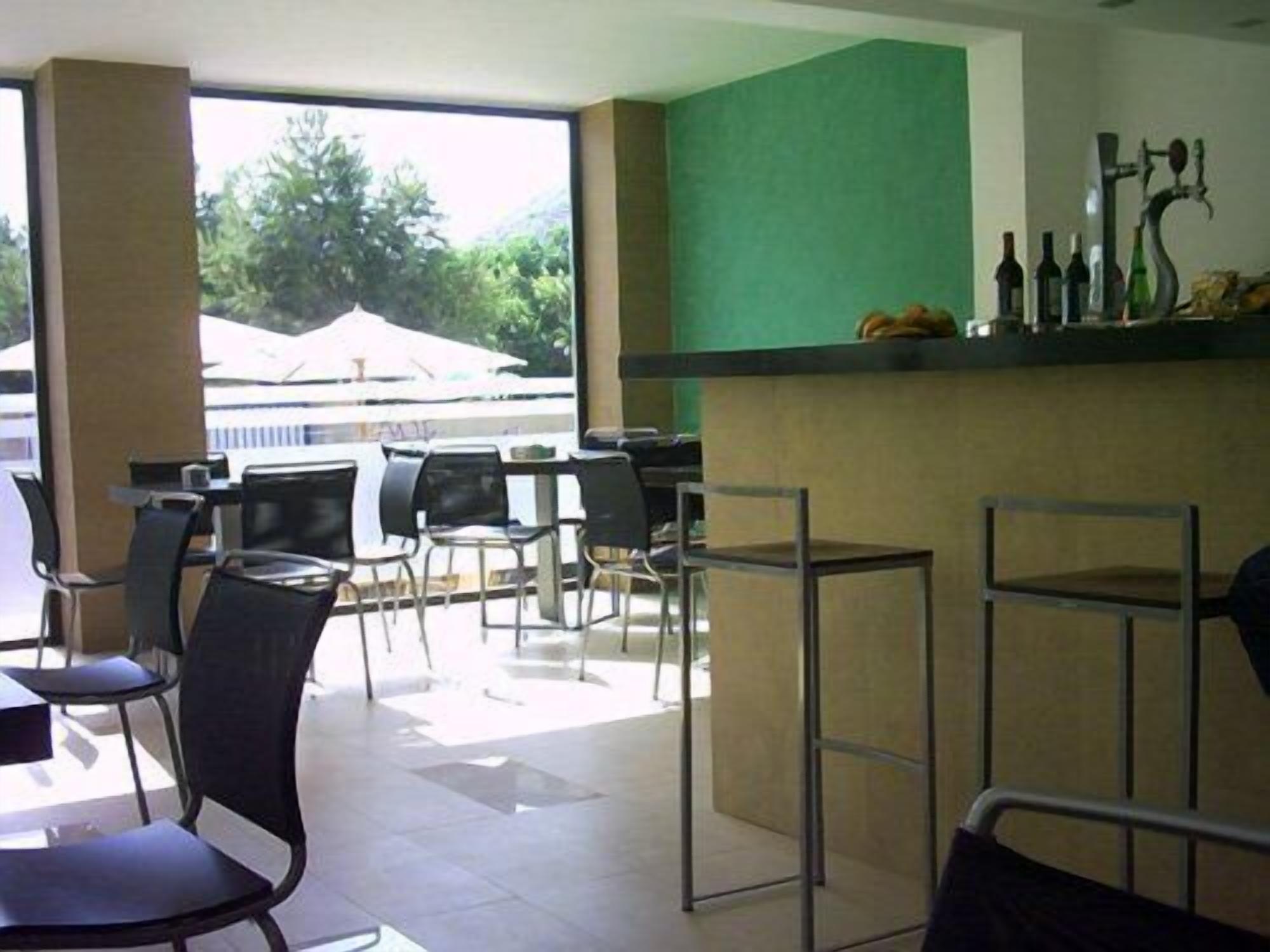 A restaurant with outdoor seating, a counter with bottles, and a view of trees and a building outside.