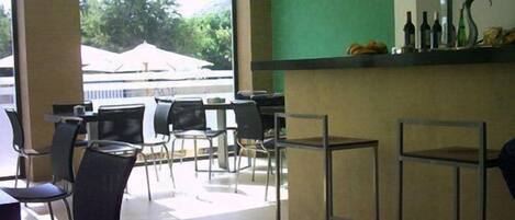 A restaurant with outdoor seating, a counter with bottles, and a view of trees and a building outside.