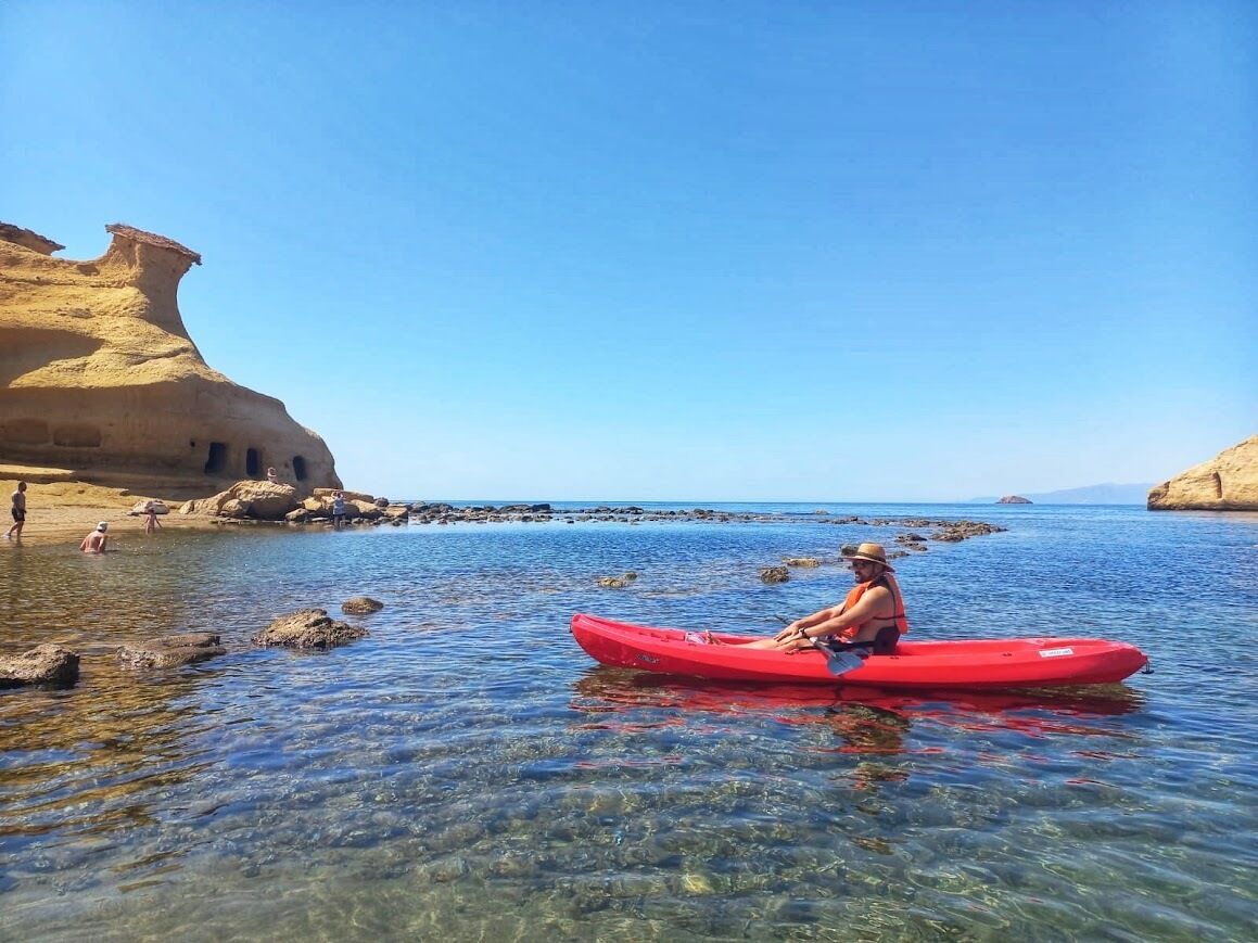 Una persona en kayak sobre aguas claras con formaciones rocosas a los lados.