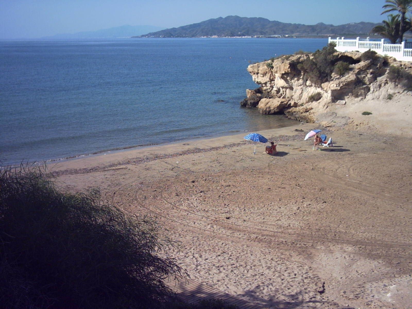 Une plage avec une falaise rocheuse, un palmier et deux parasols.