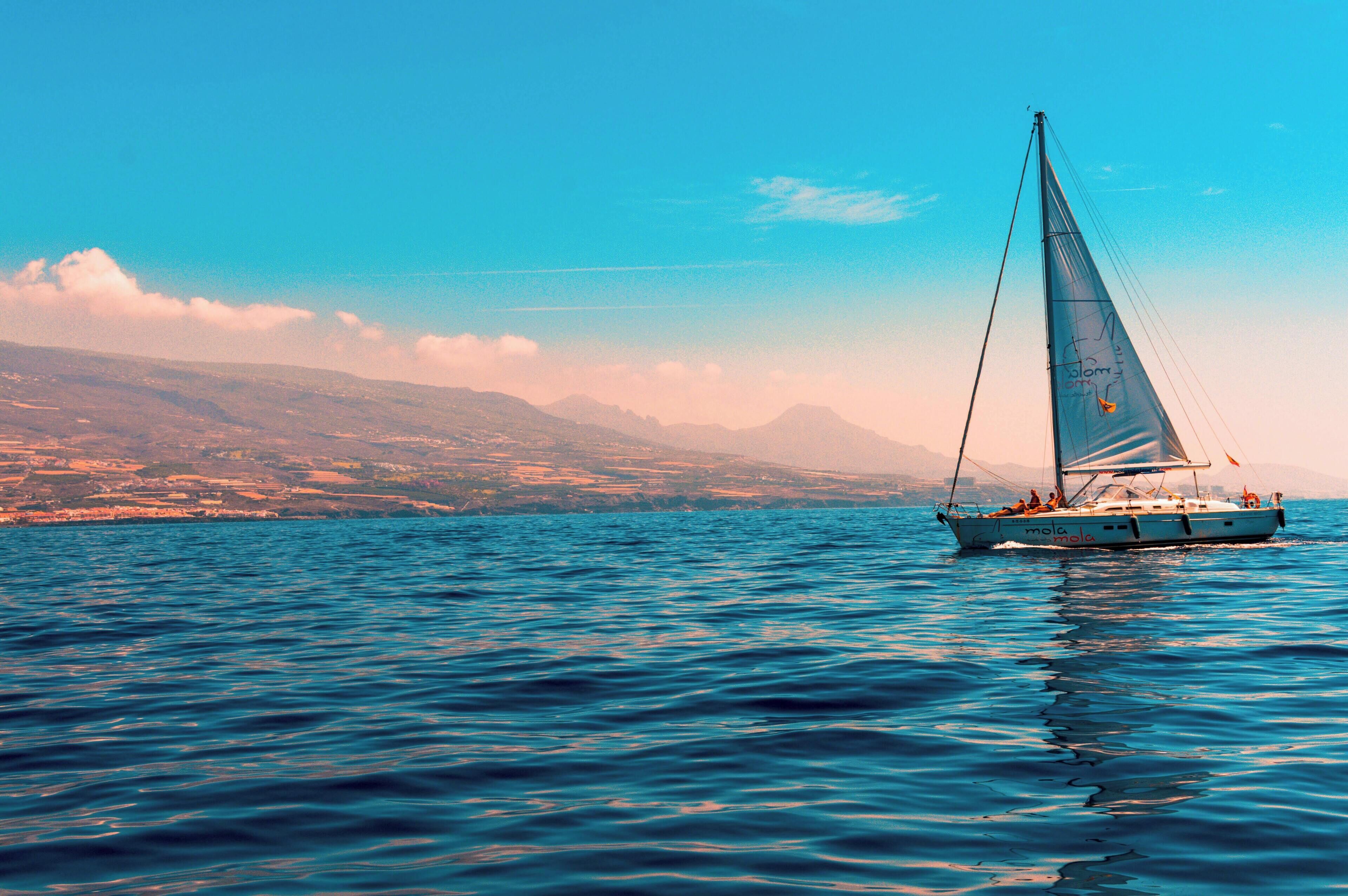A sailboat on a calm sea with a mountainous coastline in the background.