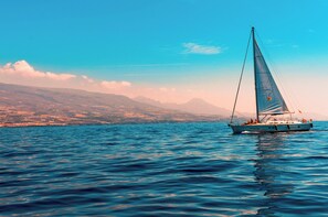 A sailboat on a calm sea with a mountainous coastline in the background.
