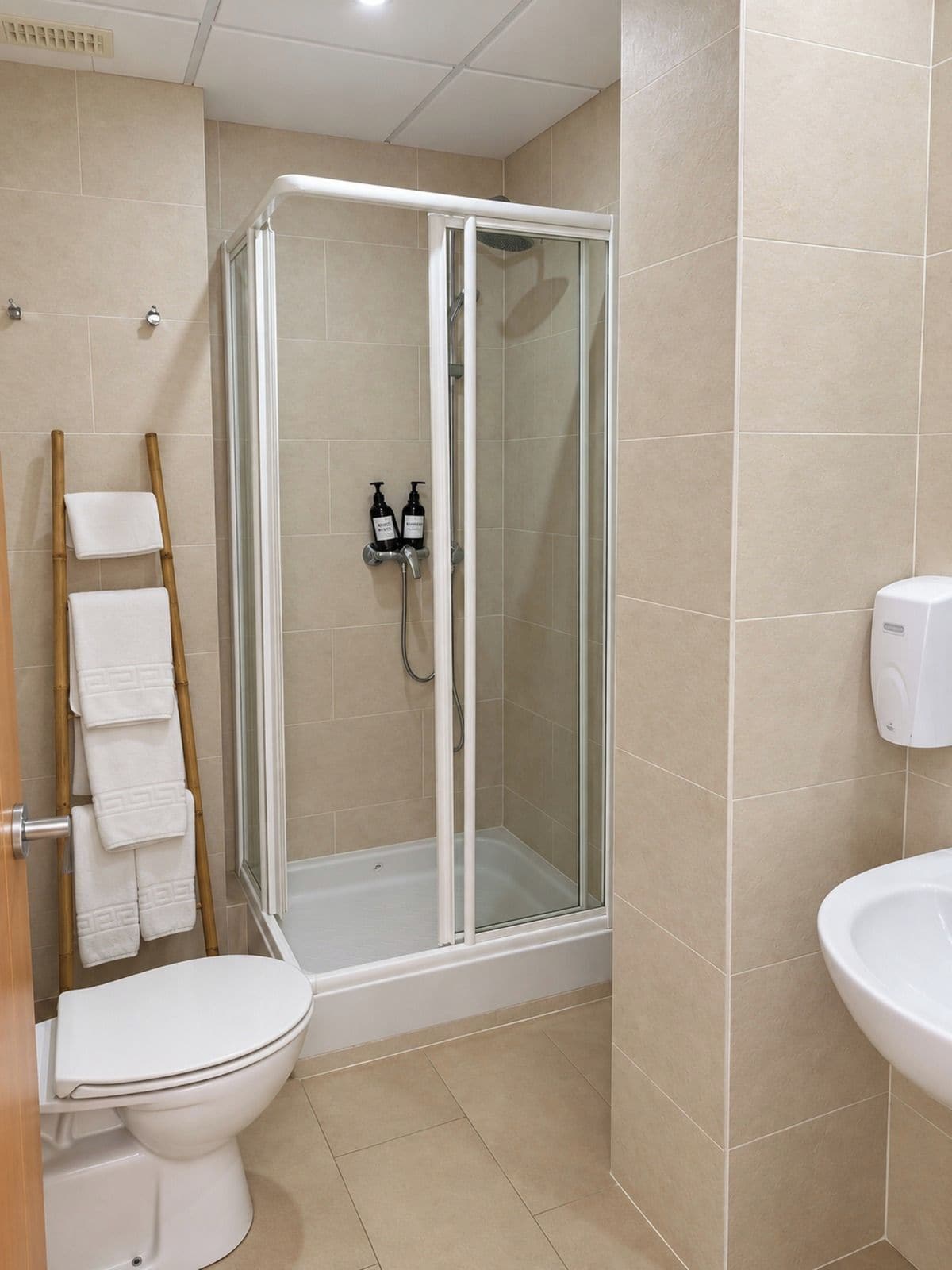 Un baño con ducha envuelta en vidrio, inodoro, lavabo y toallero con toallas dobladas.