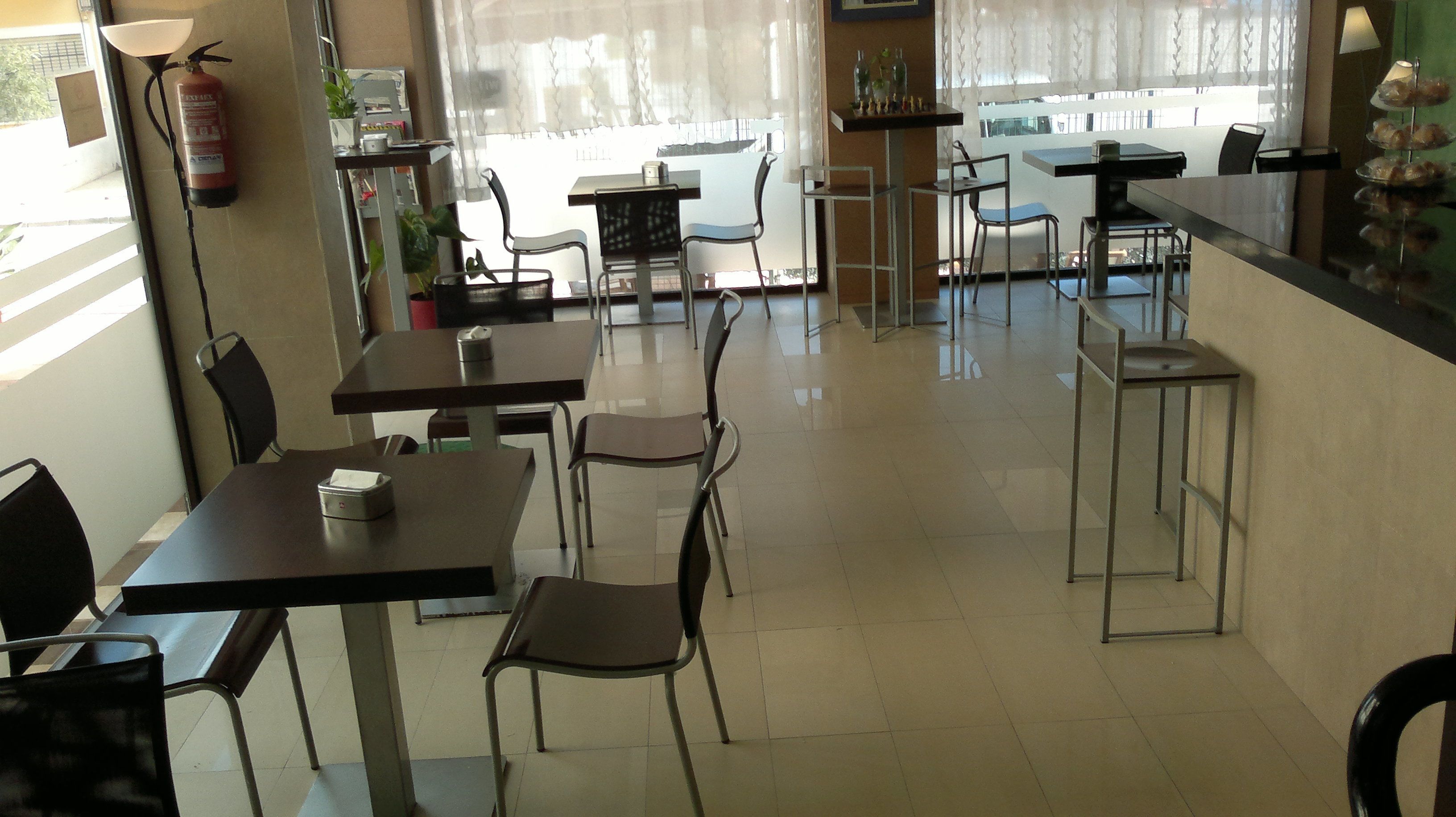 A cafe with tables and chairs, a fire extinguisher, and a window with curtains.
