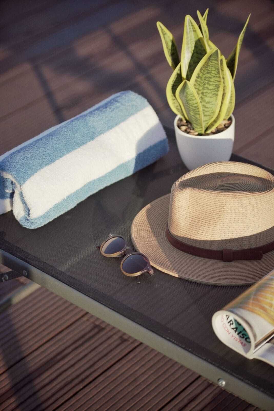 A glass table with a striped towel, a woven hat, a potted plant, and sunglasses.