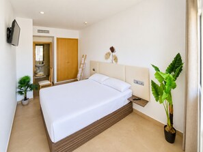 A hotel room with a large bed, a bedside table with a remote control, a wall-mounted TV, a wooden wardrobe, a bathroom with a sink and mirror, and two potted plants. - Hotel Playa Terreros by Blossom Hotels (Pulpi)