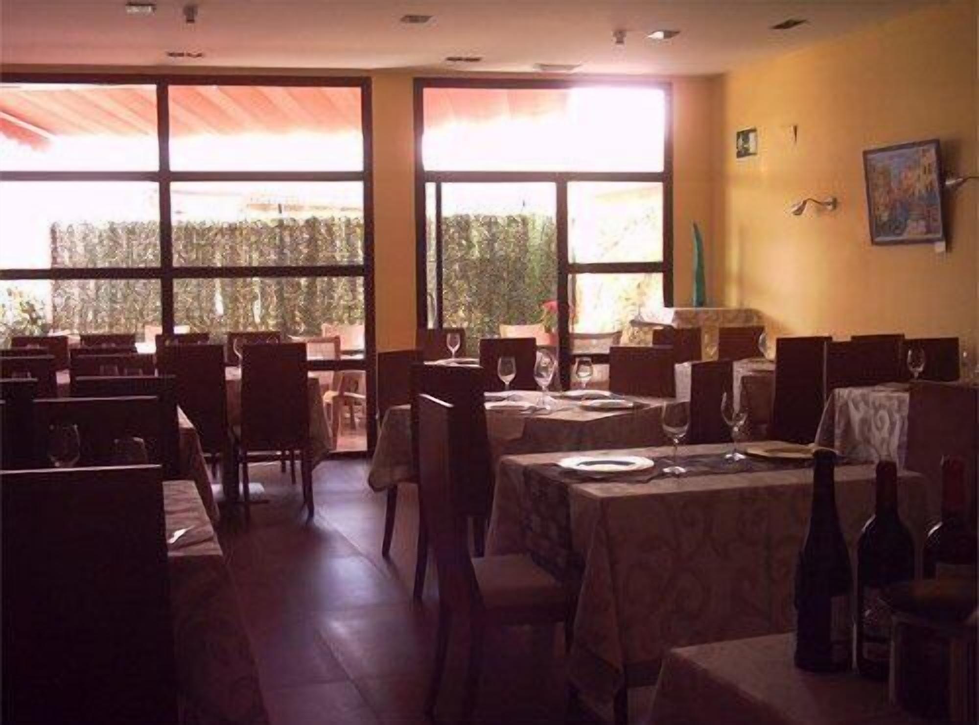 A restaurant with multiple tables and chairs, large windows, and a view of trees outside.