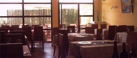 Un restaurant amb diverses taules i cadires, grans finestres i vista als arbres.