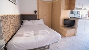 A neatly made bed with white linens and two folded towels, a television on a wooden stand, and a wardrobe with a mirror. - Italianway   - Bligny 39 (Milan)
