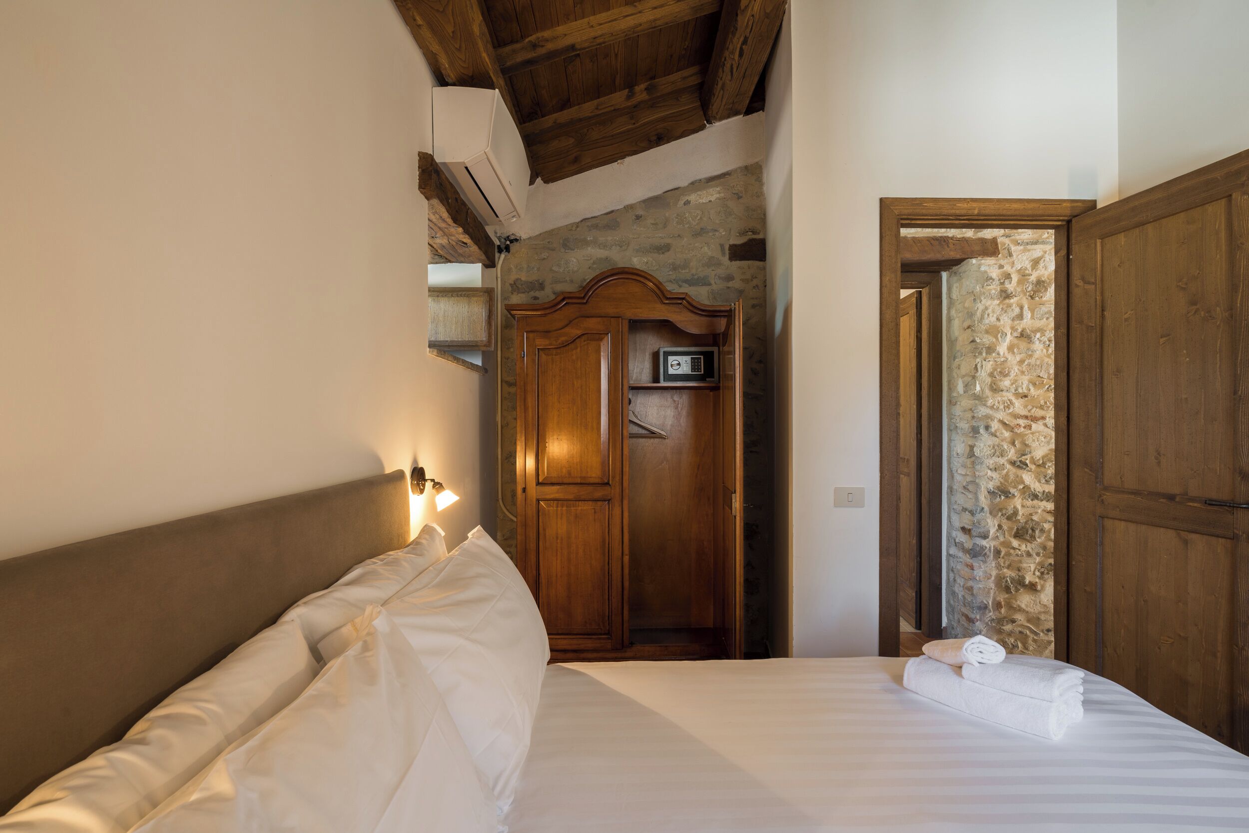 A bedroom with a wooden headboard, a bed with white linens, a nightstand with a lamp, and a wooden wardrobe.