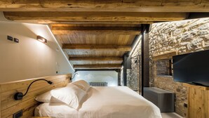 A bedroom with a wooden ceiling, stone wall, and a flat-screen TV mounted on the wall. - Borgotufi Albergo Diffuso (Castel del Giudice)