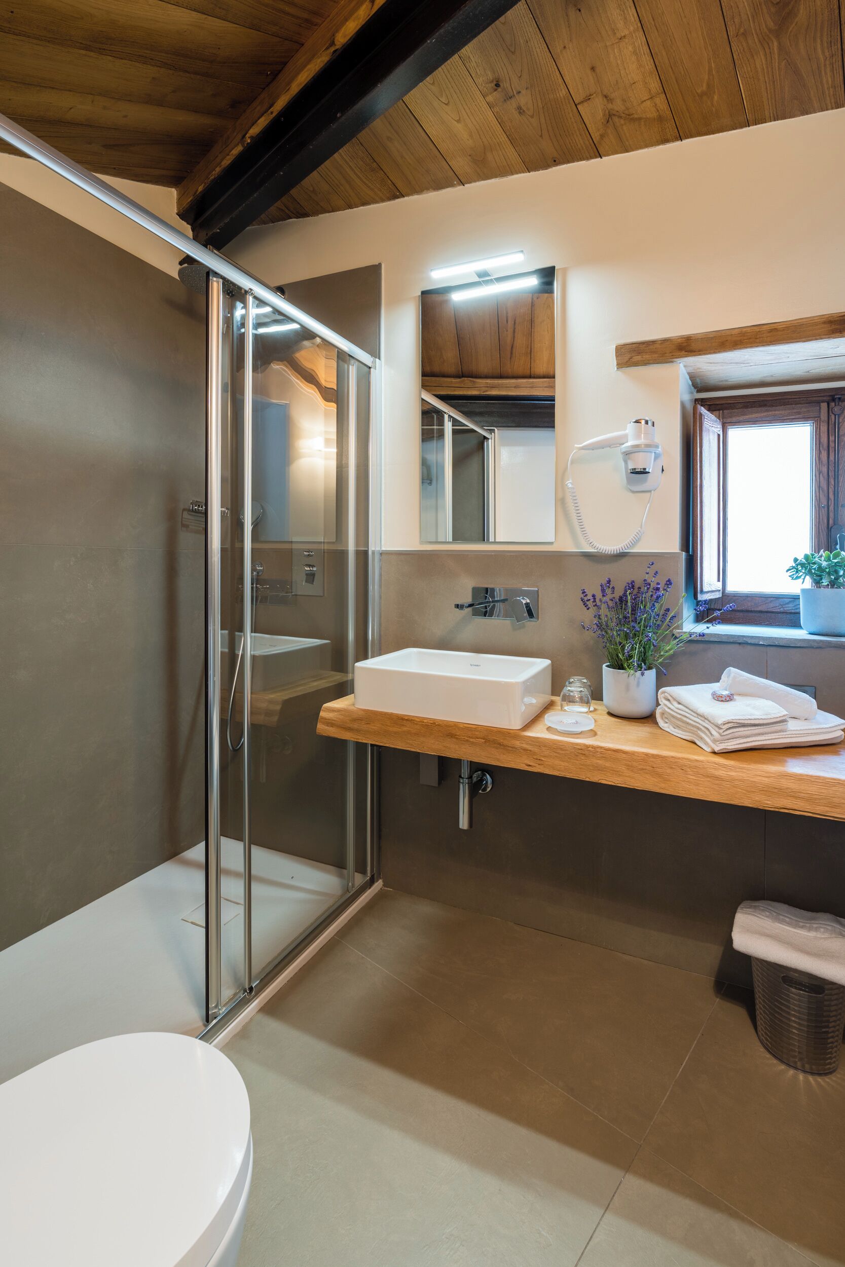 A modern bathroom with a glass shower enclosure, a white sink, and a wooden countertop.