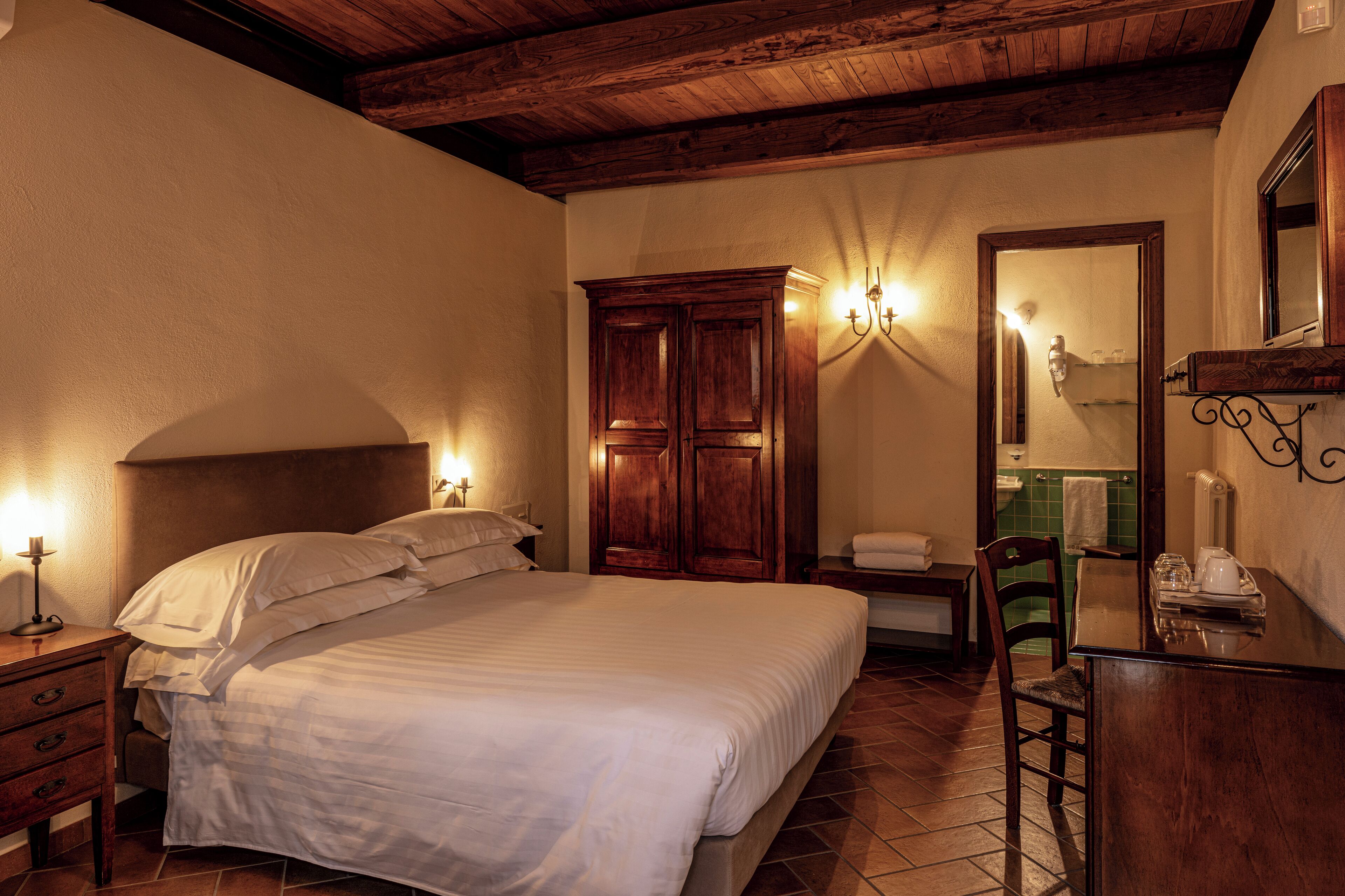 A bedroom with a large bed, wooden wardrobe, and a small table with a chair.