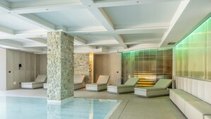A modern indoor pool area with lounge chairs, a stone pillar, and a glass-enclosed spa area. - Borgotufi Albergo Diffuso (Castel del Giudice)