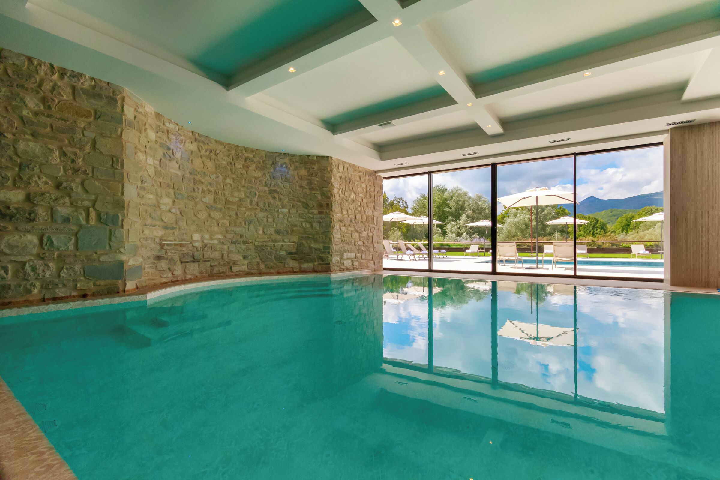 Piscina interior com paredes de pedra e grandes janelas que oferecem vista para o exterior.