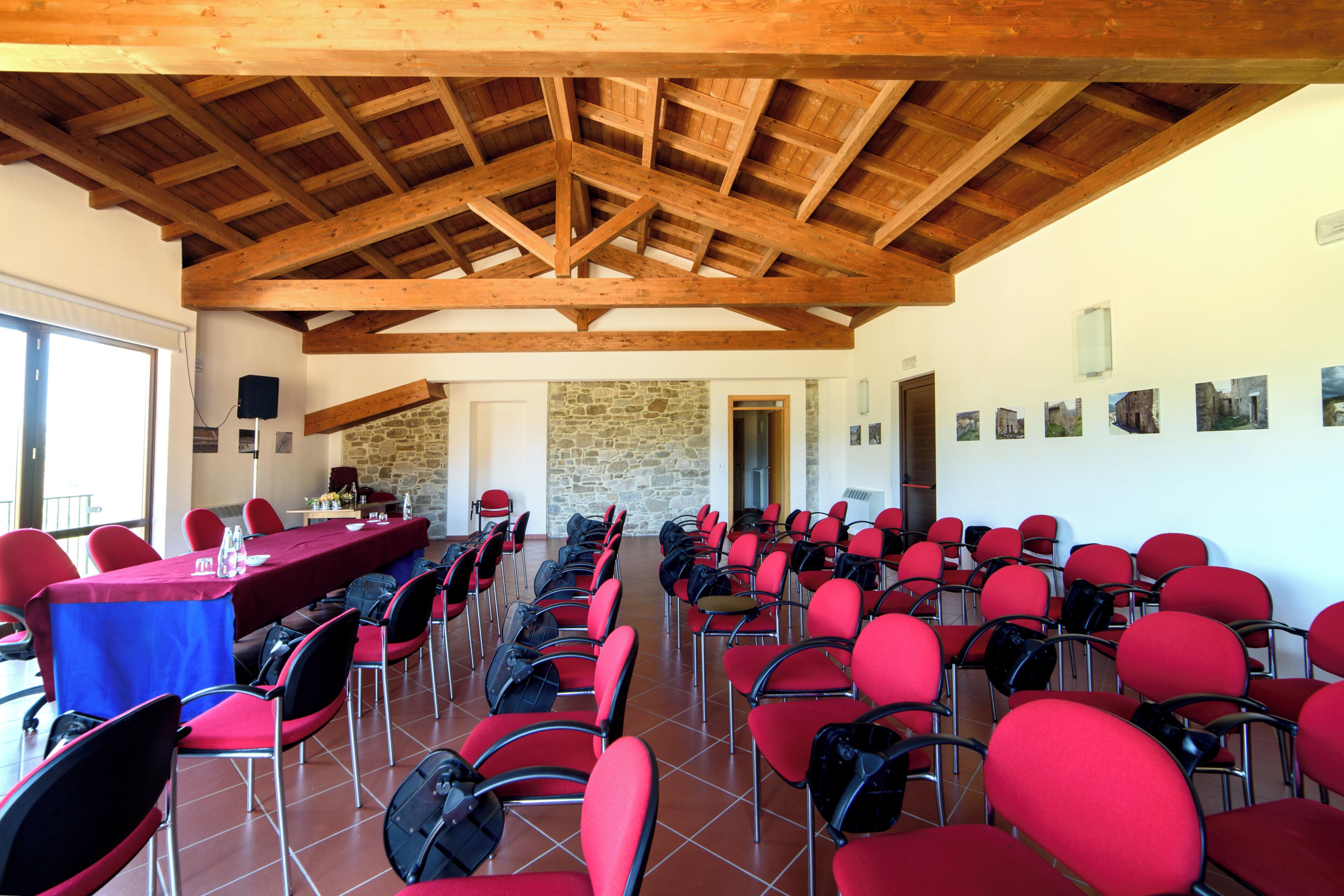 A conference room with red chairs and a long table, wooden beams on the ceiling, and a stone wall.