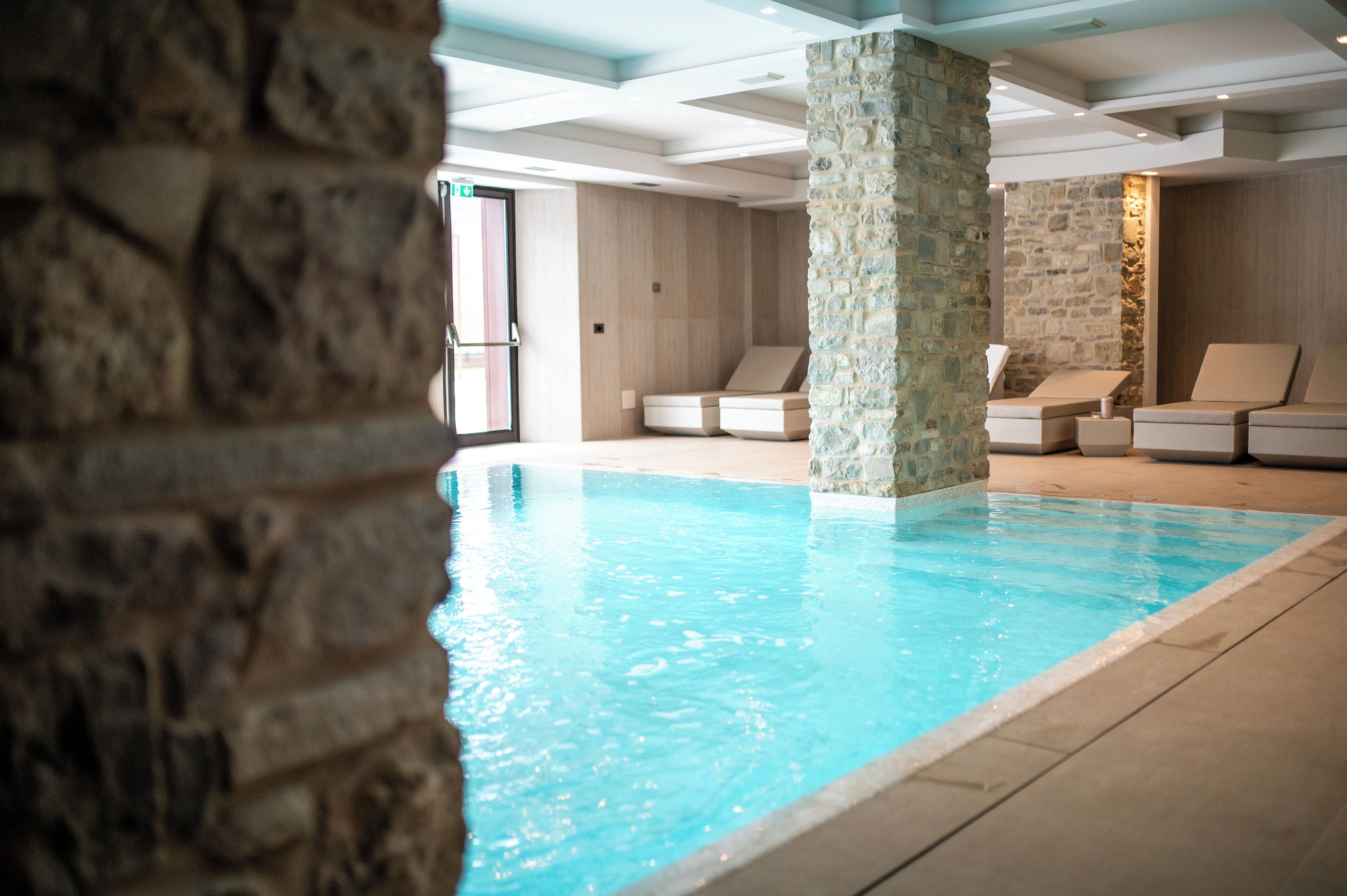 Una piscina interior con paredes de piedra y sillones de descanso.