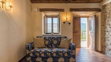 Una habitación acogedora con un sofá estampado con motivos florales, techo de madera y vistas al exterior a través de una puerta.