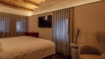 Habitación de hotel con una cama grande, un escritorio, una silla, un televisor montado en la pared y un florero con ramas sobre una mesita de noche.