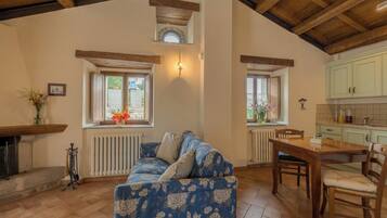 A cozy living room with a floral sofa, wooden dining table, and a kitchen area with light green cabinets.