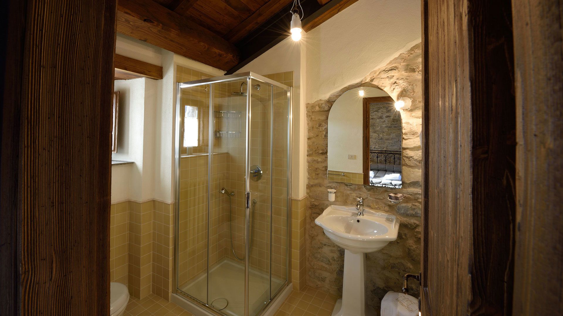 Un baño con cabina de ducha de vidrio, lavamanos pedestal y pared decorativa de piedra.