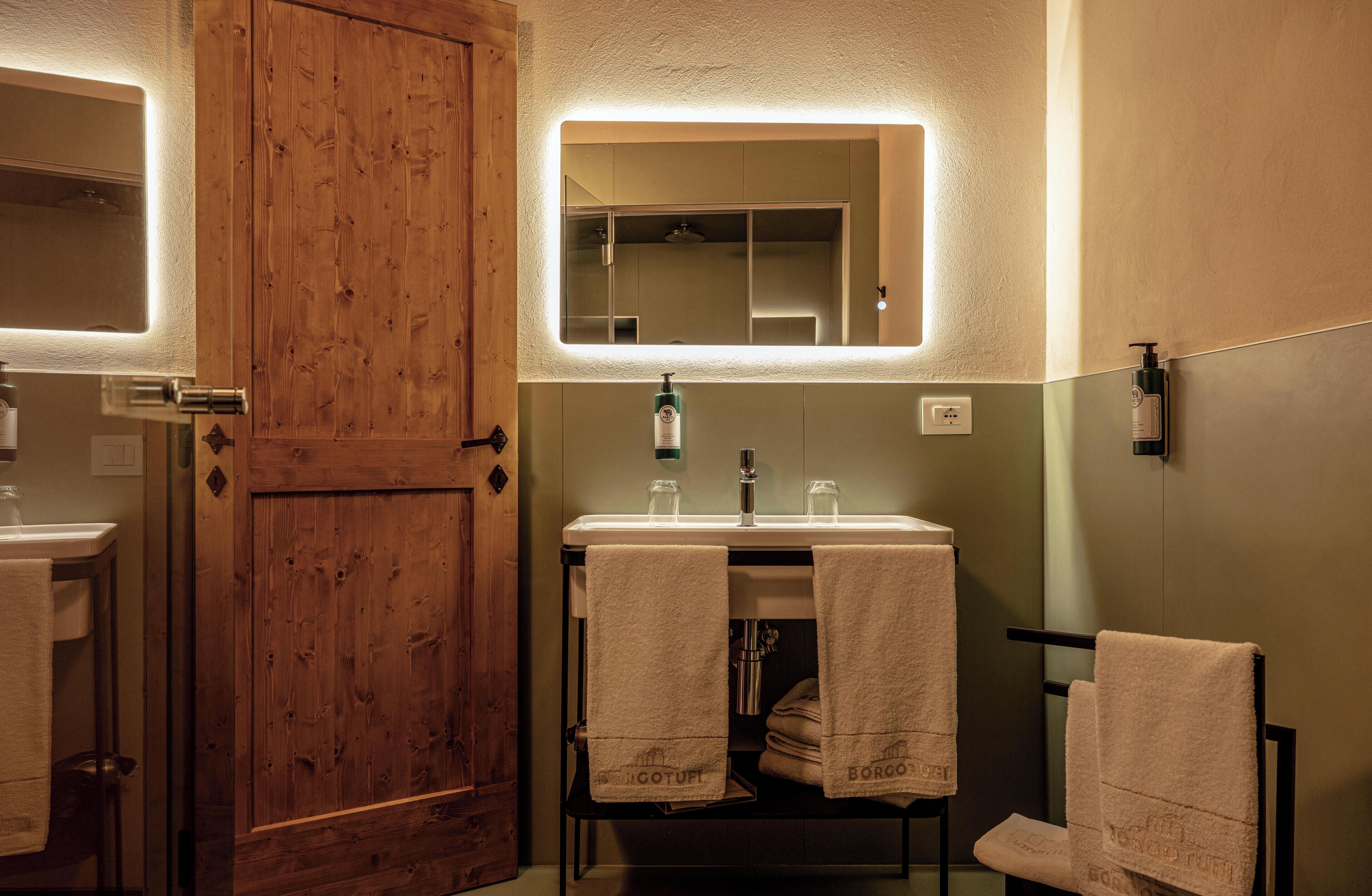 Une salle de bain avec une porte en bois, un miroir, un lavabo avec deux serviettes et un flacon de savon.