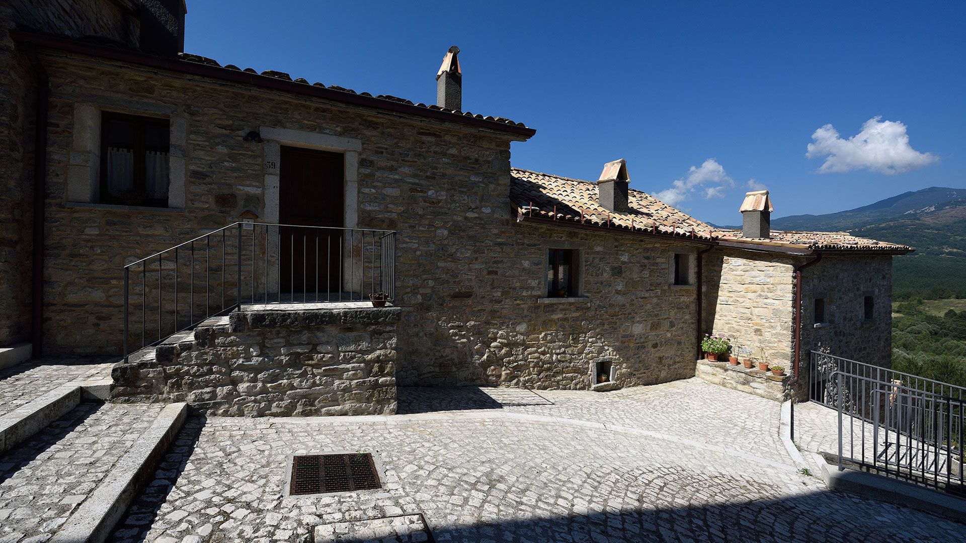 A stone building with a tiled roof, a small balcony, and a cobblestone courtyard.