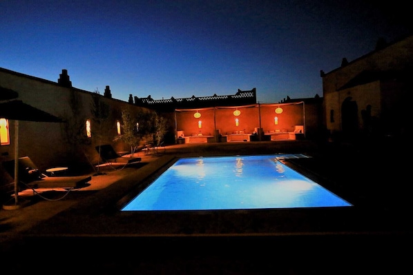 Una piscina con sillas de descanso y un espacio de estar, rodeada de muros con ventanas y una cerca.