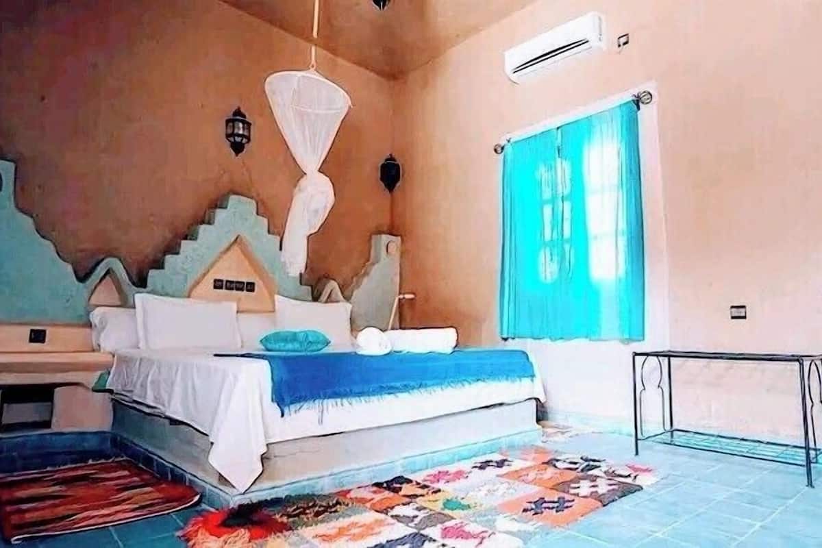 A bedroom with a bed, a nightstand, a window with curtains, a wall-mounted air conditioner, and a patterned rug.