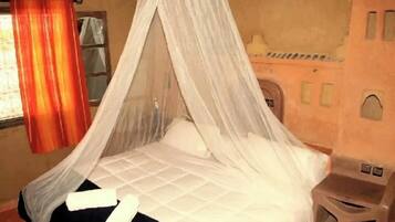A room with a bed under a canopy, a window with curtains, and a small stool.
