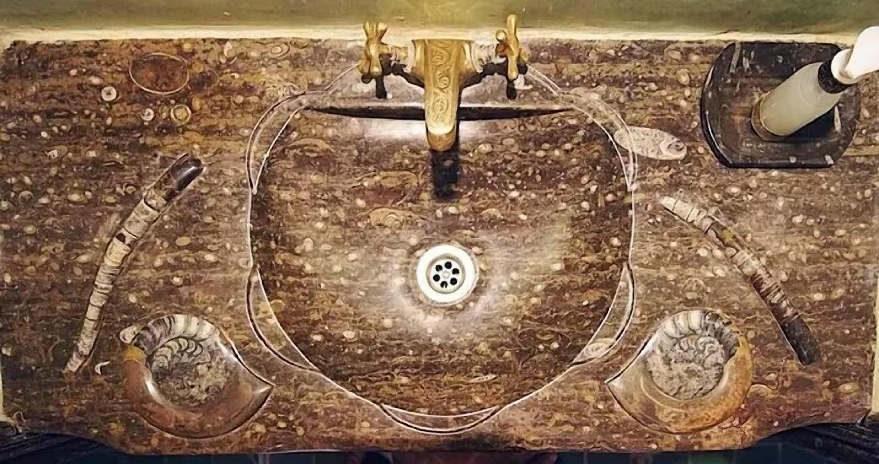A marble sink with a drain, two faucets, and a soap dispenser.