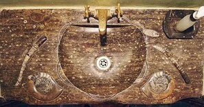 Un lavabo de mármol con desagüe, dos grifos y dispensador de jabón.