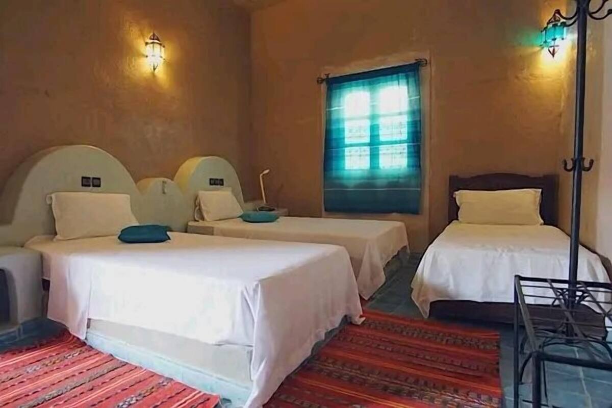 A hotel room with two beds, a small table, and a window with a view.