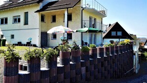 A two-story building with a balcony, a small outdoor seating area with an umbrella, and a wooden fence. - Ferienwohnungen nähe Badesee (Bergneustadt)