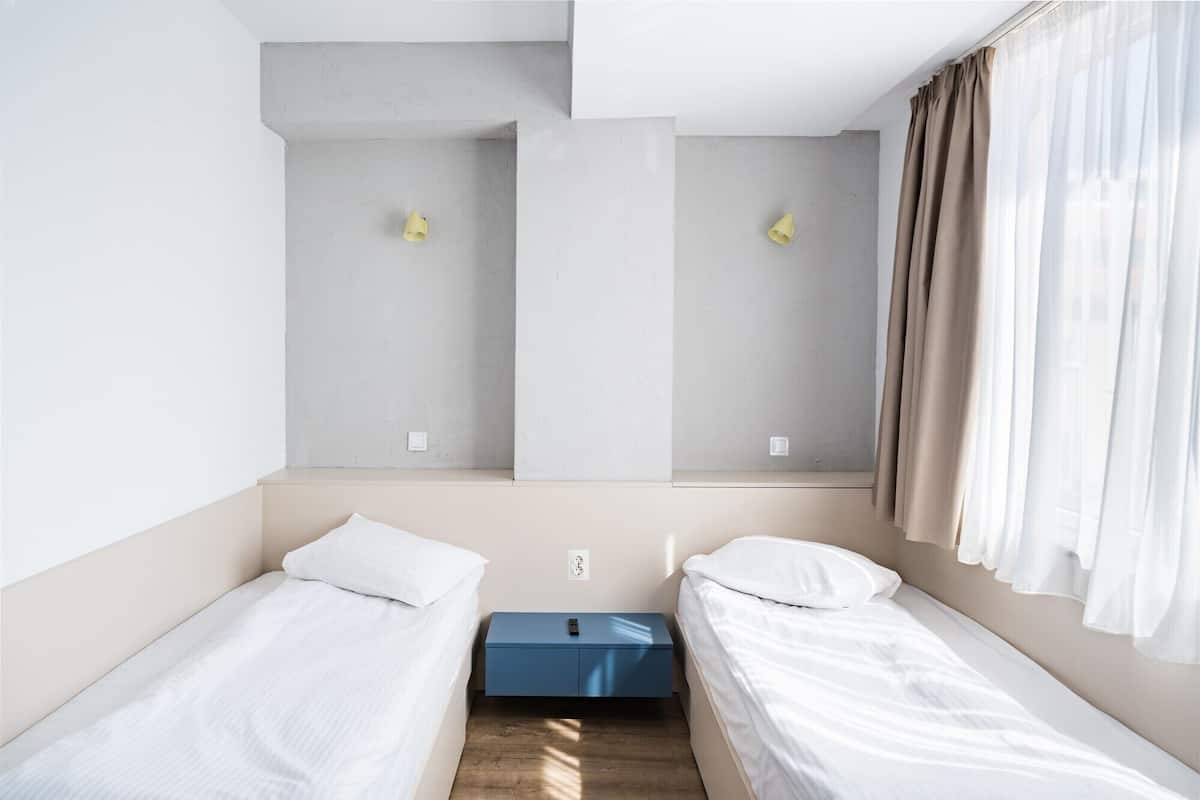 Een strak ingerichte hotelkamer met twee eenpersoonsbedden, een klein bureau en een raam met gordijnen.