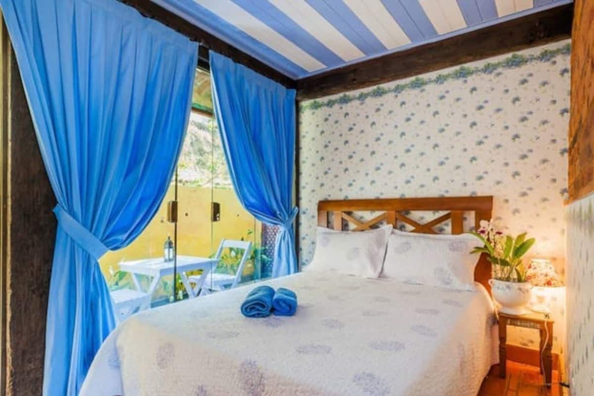 Un dormitorio con cama, cortinas, mesita de noche y ventana.