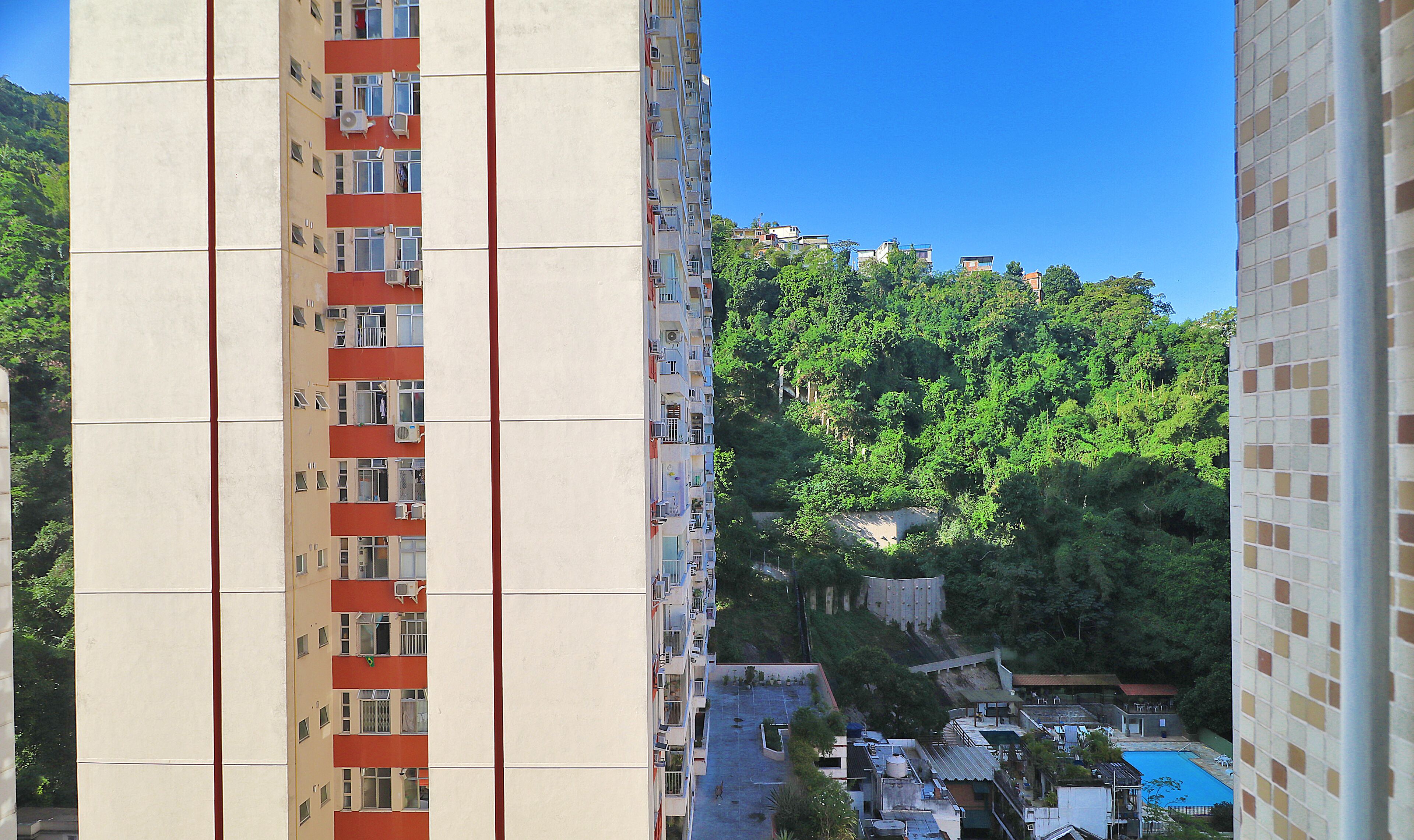 Un immeuble de grande hauteur doté de nombreux balcons, d’une piscine sur le toit et, en arrière-plan, d’une colline densément boisée.