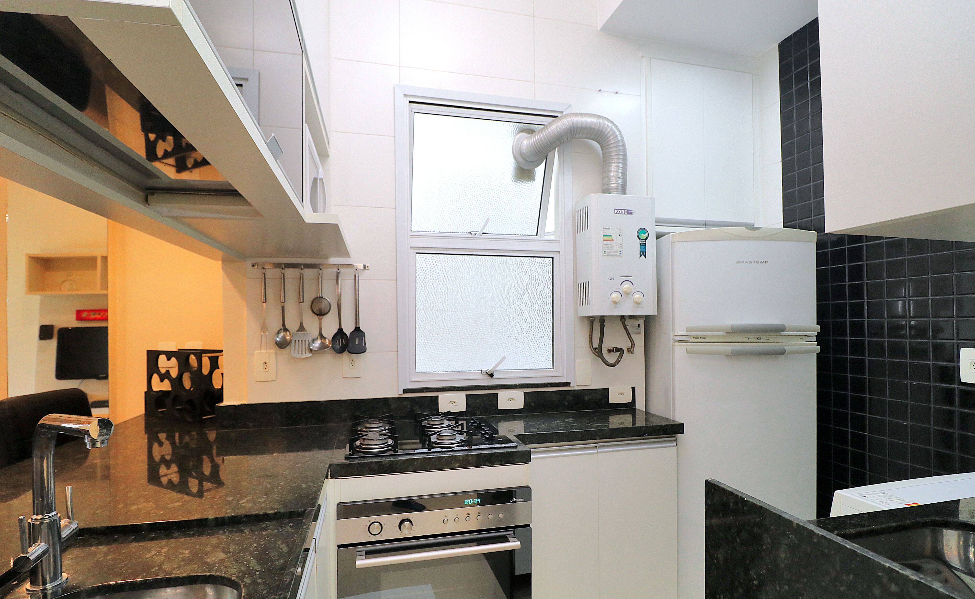 Cocina moderna con estufa a gas, horno y refrigerador empotrado. Hay una ventana con vistas al exterior, y utensilios de cocina colgados en la pared.